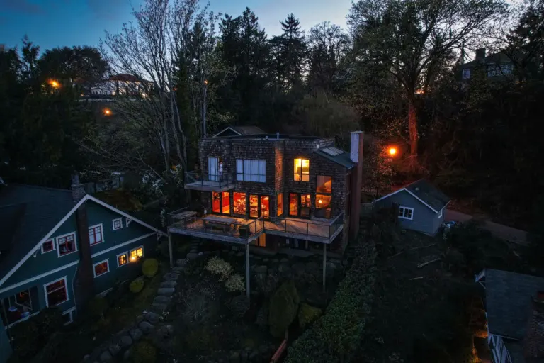 Aerial view of homes among tall evergreen trees with lights on at twilight