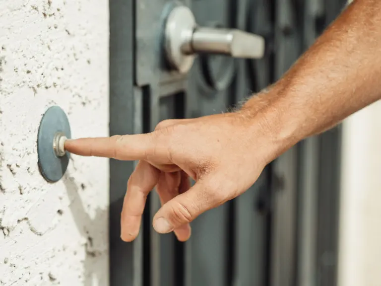 Hand pressing a doorbell outside a modern front door