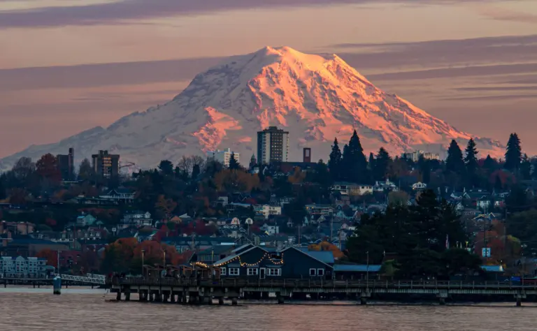 Snowcapped Mount Rainier rising above a waterfront city at sunset